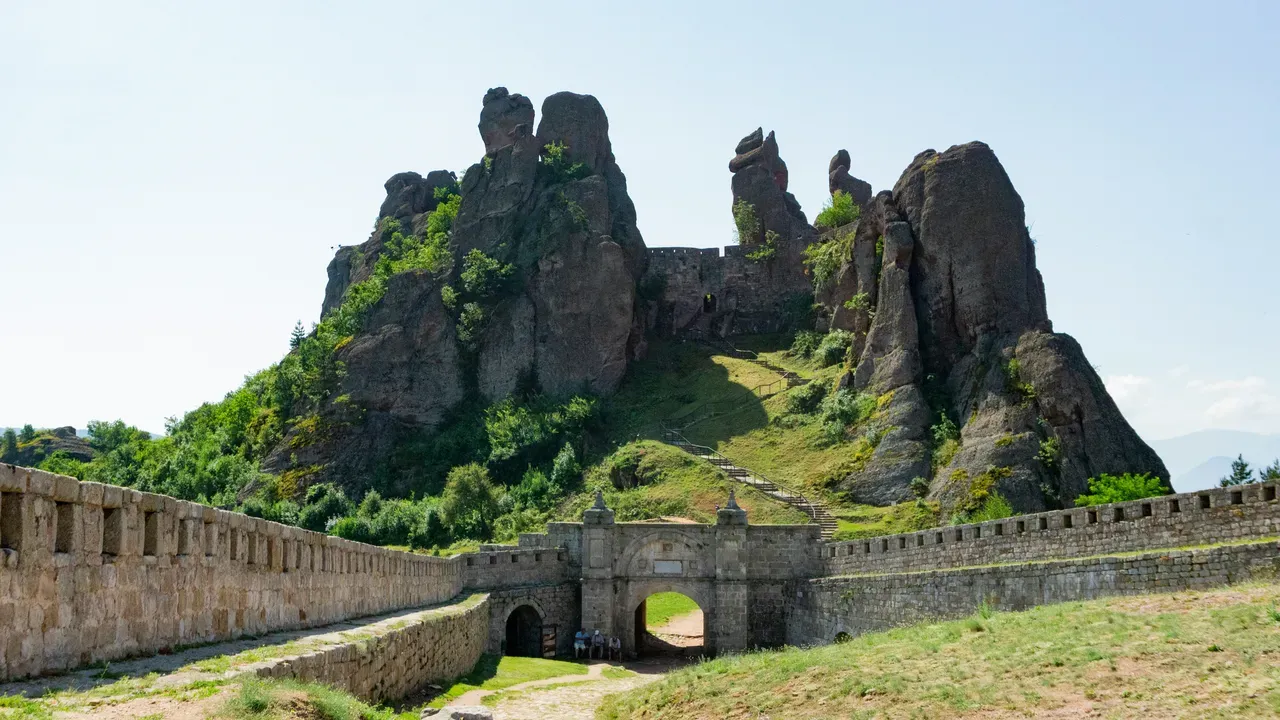 A stone fortress gate below towering rock pinnacles on a green hillside in north-western Bulgaria