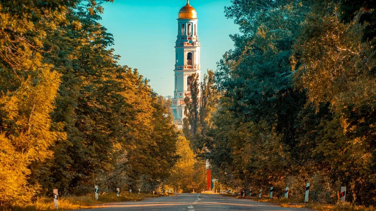 A country road lined with autumn trees leading toward a tall monastery bell tower in Moldova