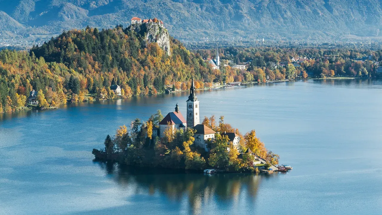 Lake Bled with its island church and clifftop castle, ringed by autumn woodland and the snow-dusted Julian Alps in Slovenia