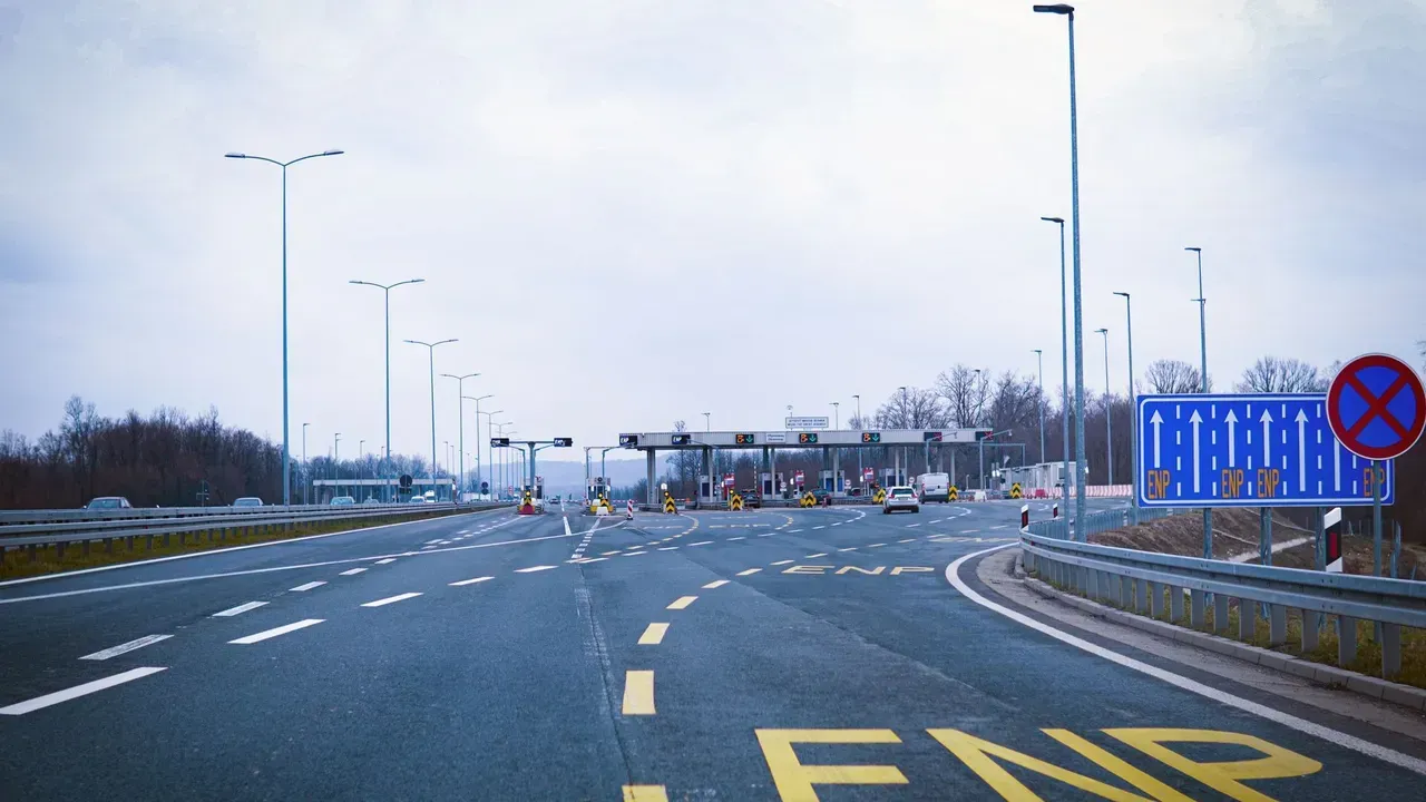 A European motorway toll plaza with overhead electronic-toll gantries and empty marked lanes under a grey sky