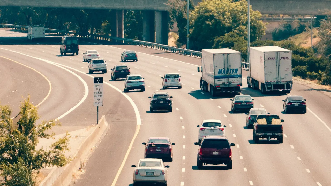 A multi-lane motorway with cars and trucks moving under a bright sky