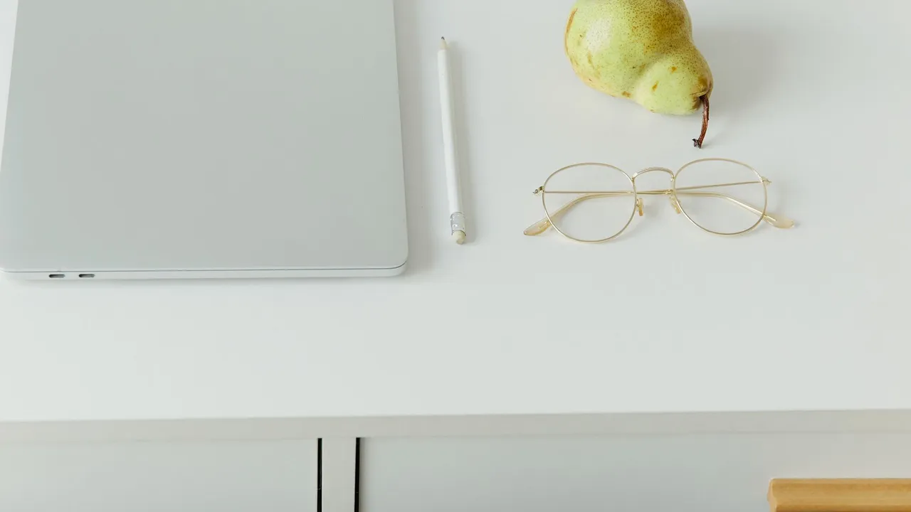 A minimal desk with a laptop, glasses, and notebook on a white surface
