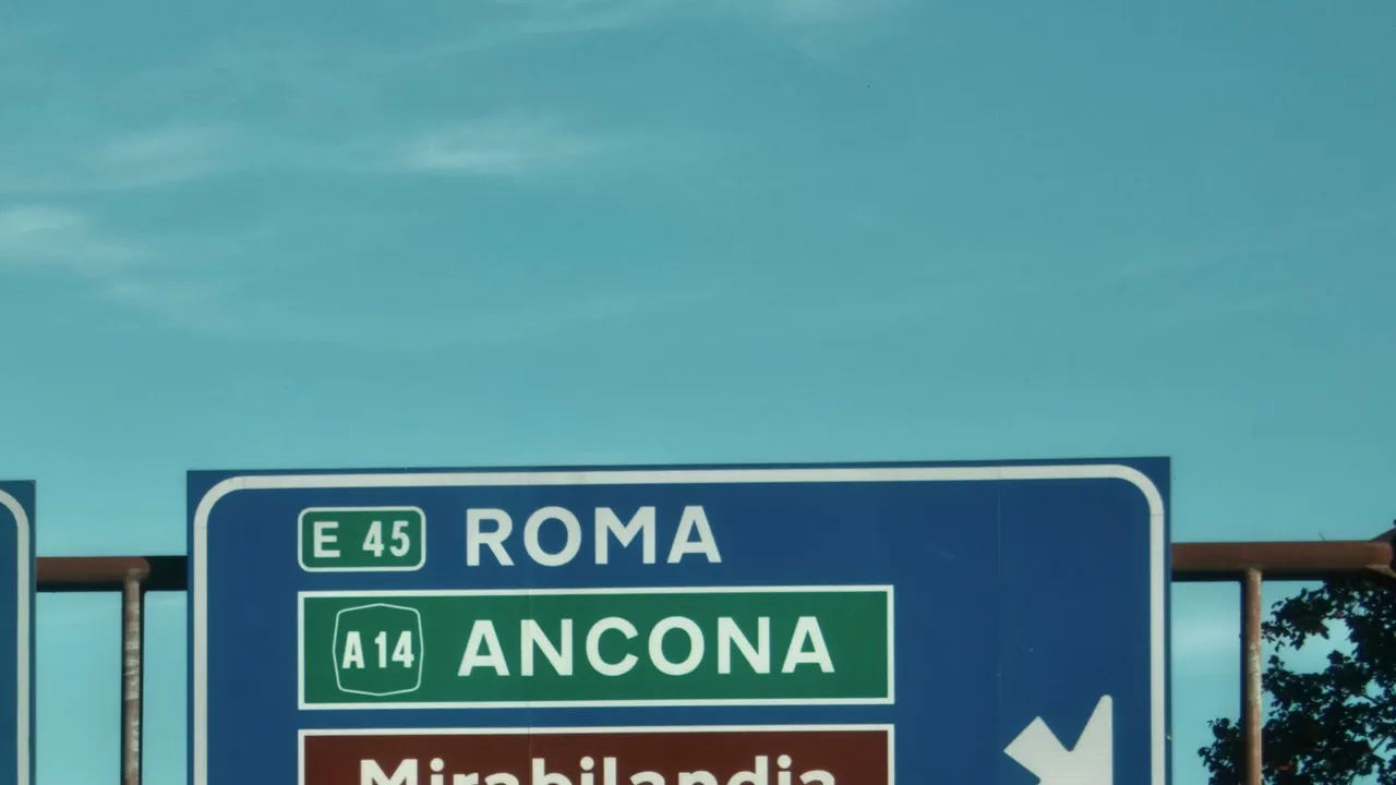 An Italian motorway sign pointing towards Roma and Ancona under a clear sky