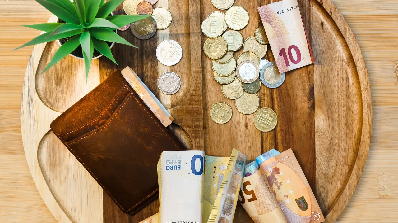 Ein Portemonnaie, Euro-Banknoten und Münzen auf einem Holztablett